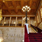 Ornate marble hall with chandeliers and a red staircase